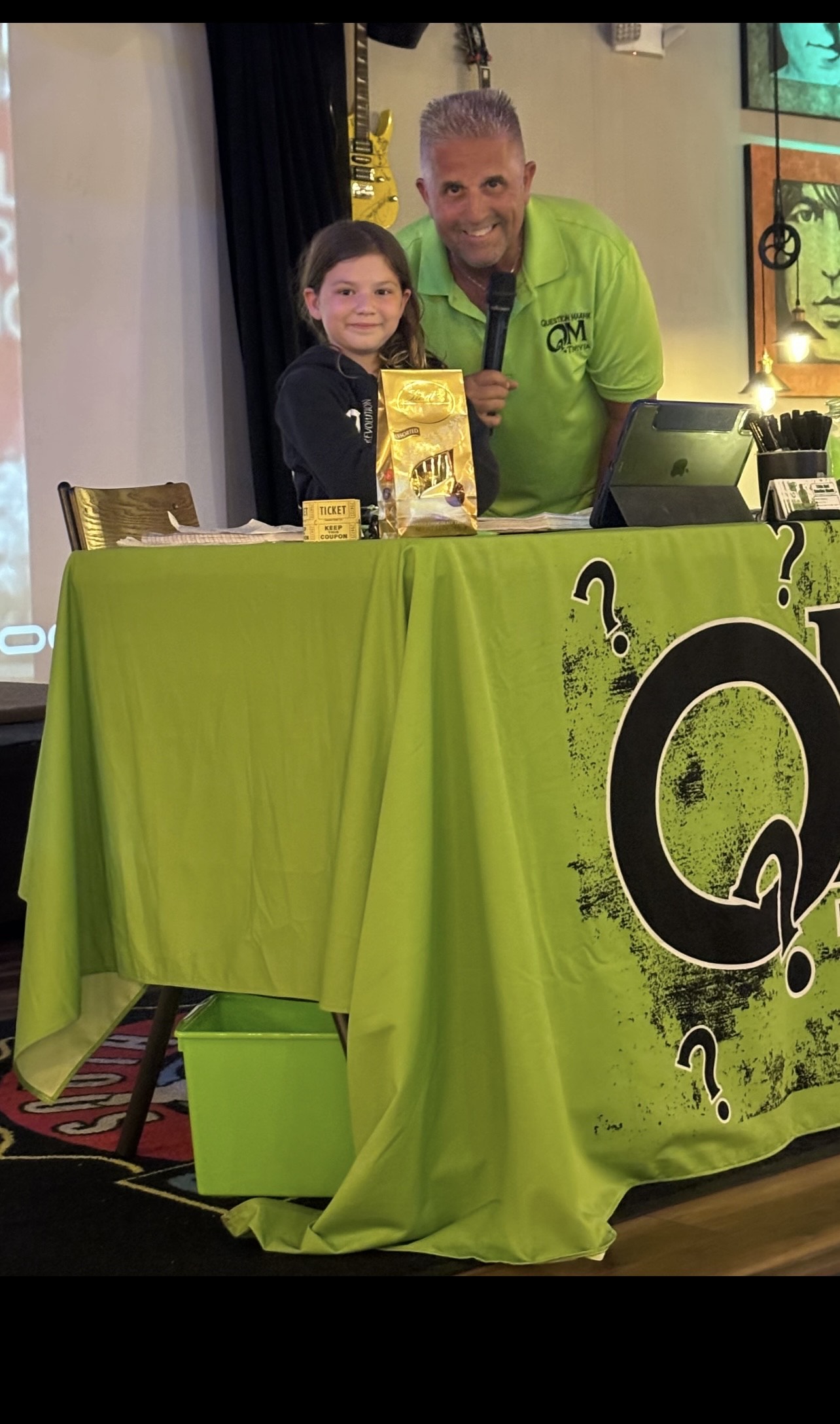 Question Maahk Trivia Host and Owner Mark Marino standing behind hosting table with young audience member.